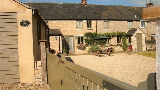 Un bâtiment en pierre doté d’un patio couvert, d’une clôture en bois et d’une enseigne indiquant qu’il s’agit d’un « COTTAGE ».