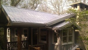 Une cabane rustique avec un toit en métal, une véranda en bois et un petit escalier menant à l’entrée.