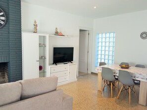 A modern living room with a flat-screen TV, a sofa, a dining table with chairs, and a decorative wall clock.
