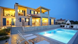 Una casa de dues plantes amb piscina, mobiliari exterior i façana de pedra.