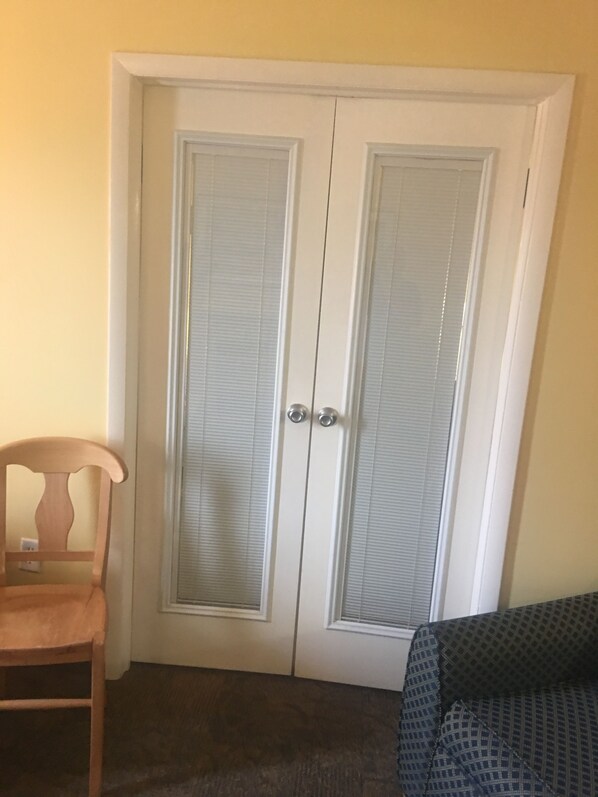 A room with a white door, a wooden chair, and a patterned sofa.