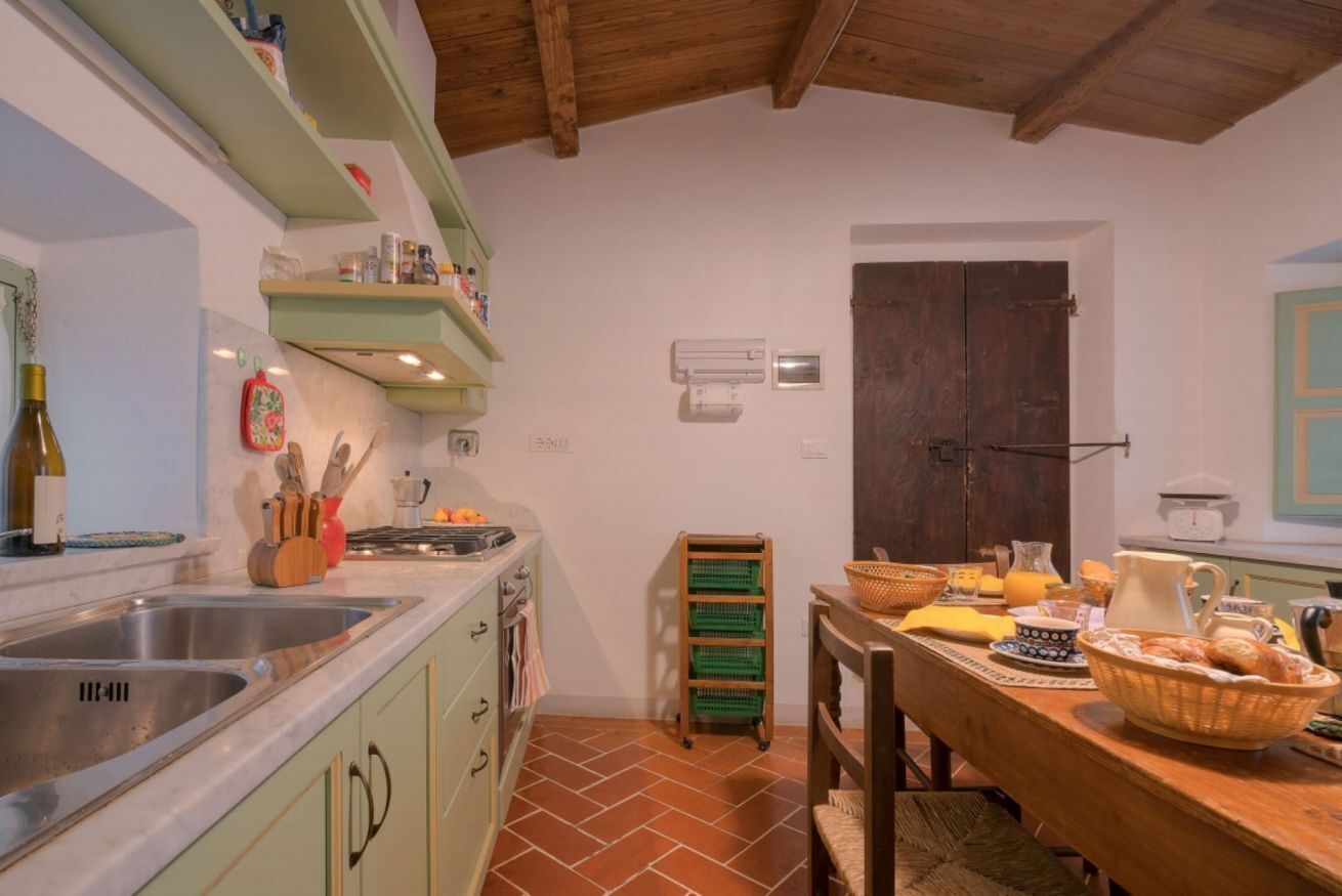 Una cocina con techo de madera, armarios verdes, un lavamanos y una zona de comedor con mesa preparada para el desayuno.