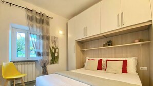 A bedroom with a bed, a chair, a window with curtains, and a wall-mounted shelf with items. - Casa Rosa, Rapallo (rapallo)