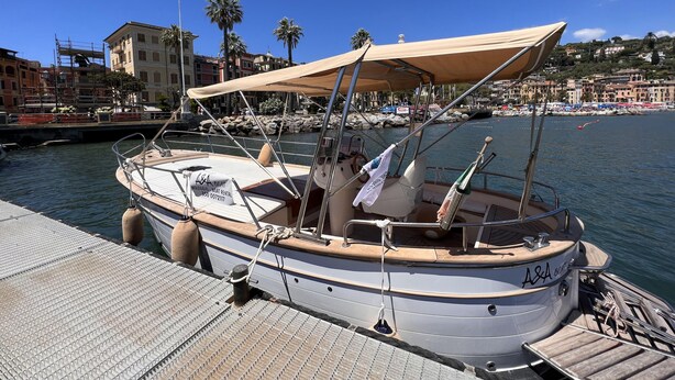 A boat docked at a pier with a covered seating area, a steering wheel, and a rope tied to a bollard. - Casa Rosa, Rapallo (rapallo)