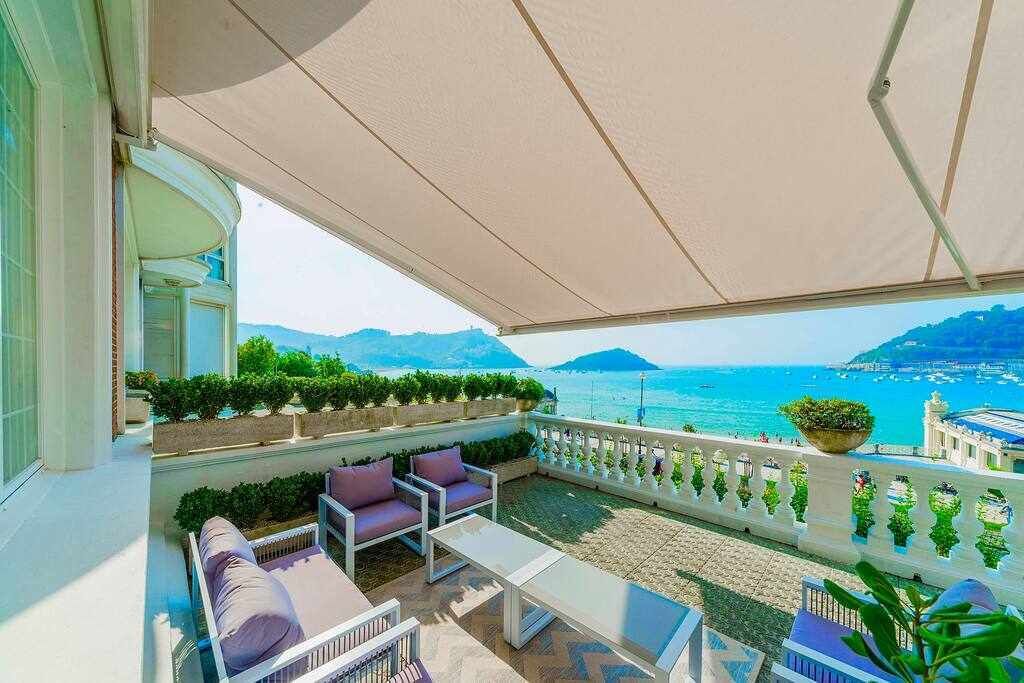Un balcon avec un espace salon extérieur, une vue sur la mer et un paysage montagneux.