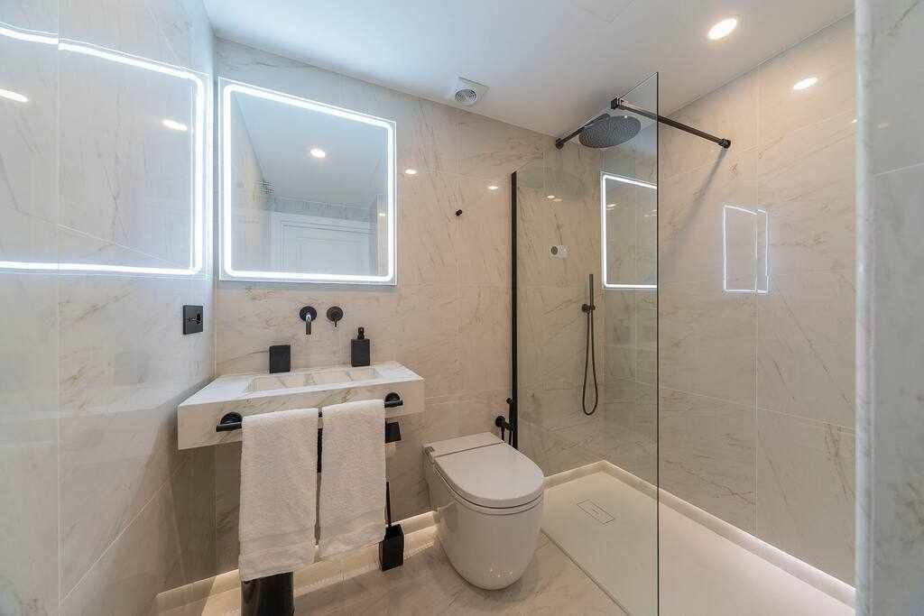 A modern bathroom with a glass-enclosed shower, a white toilet, and a vanity with a mirror and two sinks.