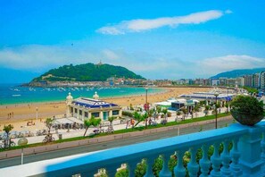 A coastal cityscape with a prominent hill, a beach, and a promenade with buildings and greenery.
