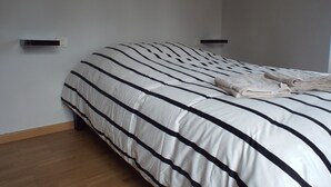 A neatly made bed with a striped bedspread, two wall-mounted night lights, and a small shelf on the wall. - Country house Near Dinard and Saint Malo (Pleurtuit)