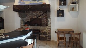 A rustic kitchen with a brick fireplace, wooden beams, and a painting of a sailboat. - Country house Near Dinard and Saint Malo (Pleurtuit)