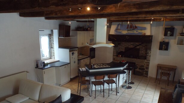 A cozy living room with a sofa, a dining table with chairs, a kitchen area with a refrigerator, and a fireplace. - Country house Near Dinard and Saint Malo (Pleurtuit)