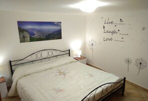 A bedroom with a bed, a nightstand, a wall-mounted lamp, and a motivational quote and dandelion illustrations on the wall.