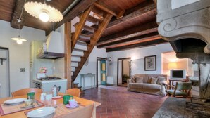 A rustic interior with exposed wooden beams, a dining area with a table set for two, a sofa, and a fireplace. - CASTLE OF SARNA Casa Cisterna  (Sarna, Chiusi della Verna)