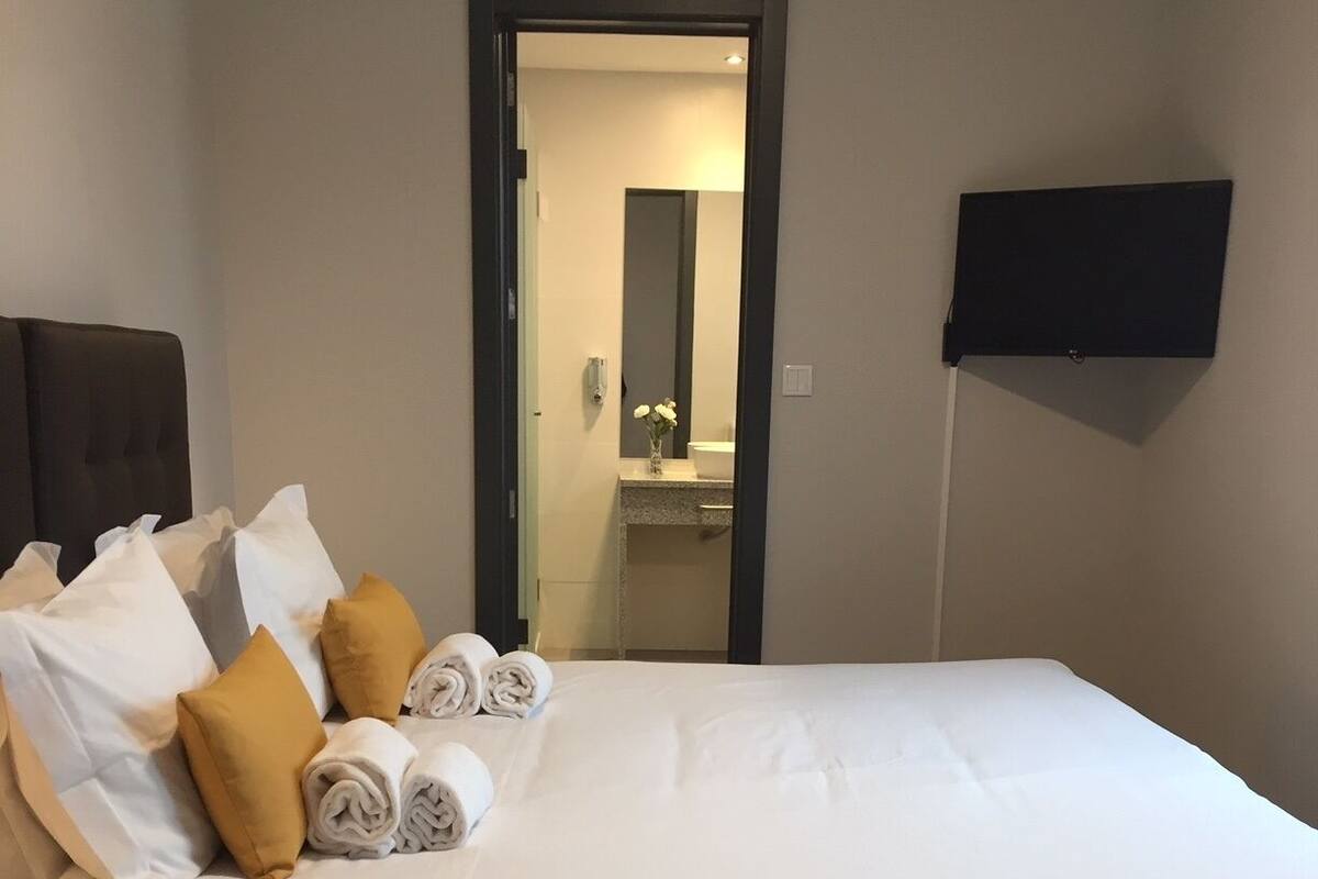 A hotel room with a bed, pillows, a TV, and a bathroom visible through an open door.