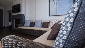 A modern living room with a sofa set, a flat-screen TV mounted above a fireplace, and a wicker chair in the foreground. - Villa Caparica Hostel (Almada)