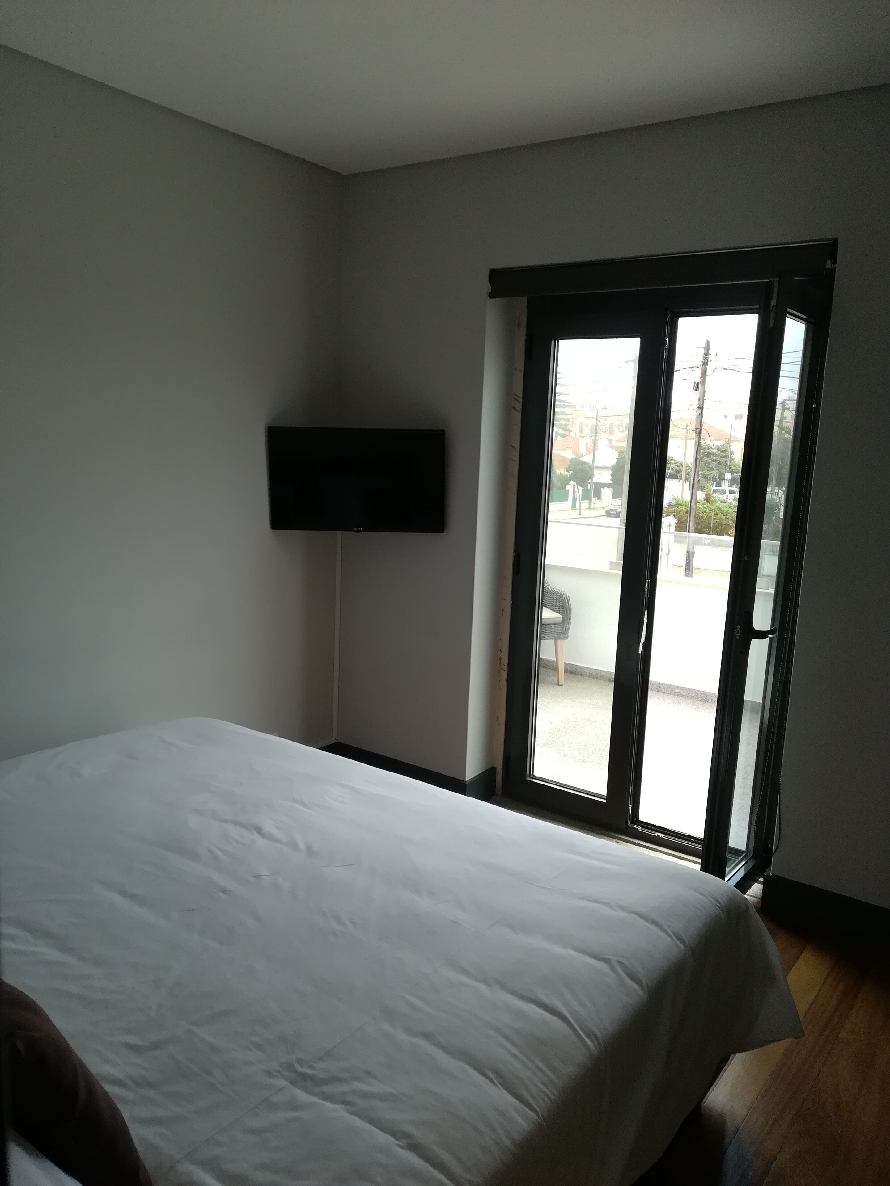 Un dormitorio con cama, televisor montado en la pared y puerta corrediza de vidrio que da a un espacio exterior.