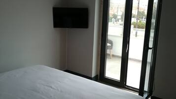 Un dormitorio con cama, televisor montado en la pared y puerta corrediza de vidrio que da a un espacio exterior.