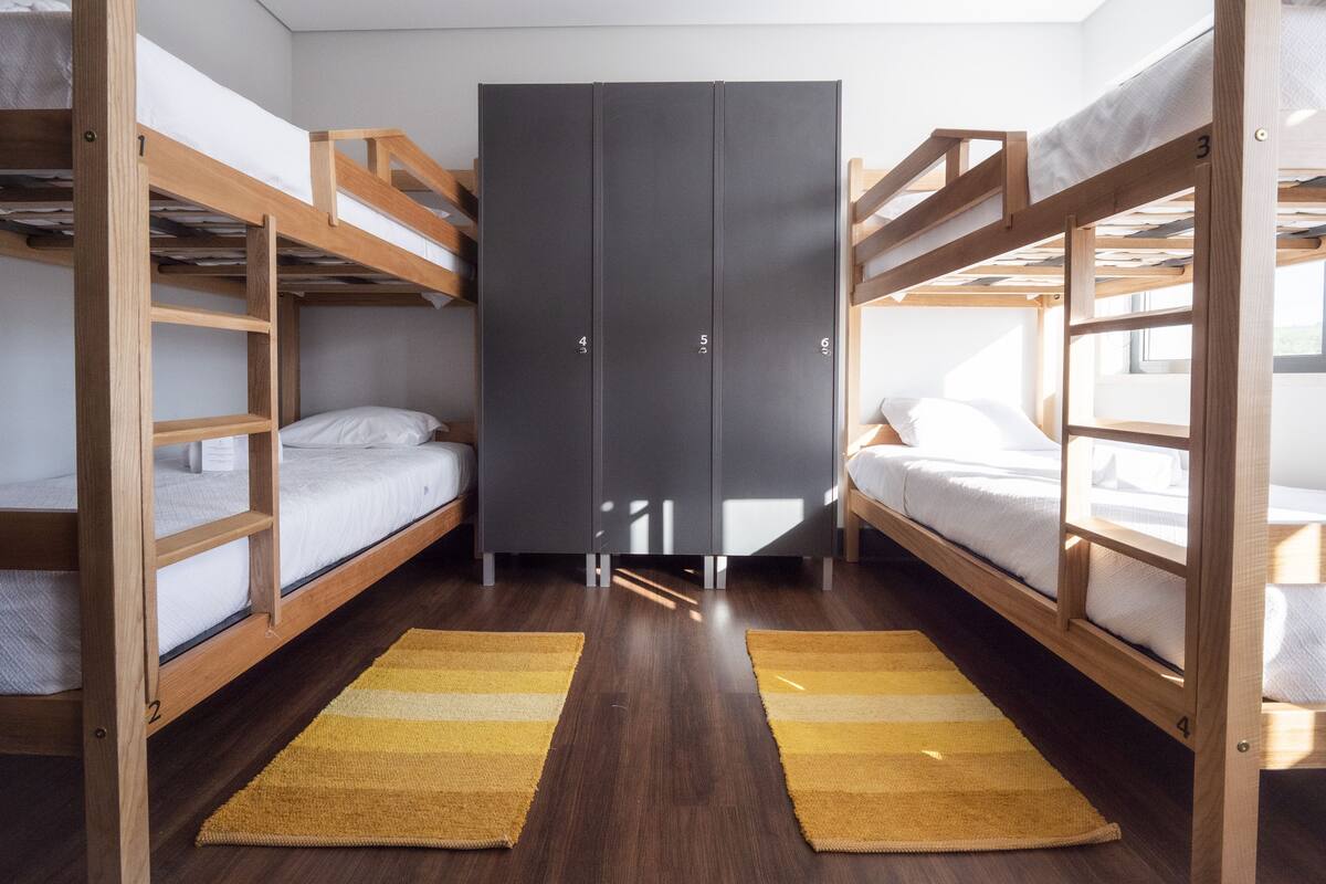 A dormitory room with bunk beds, a wardrobe, and a wooden floor.