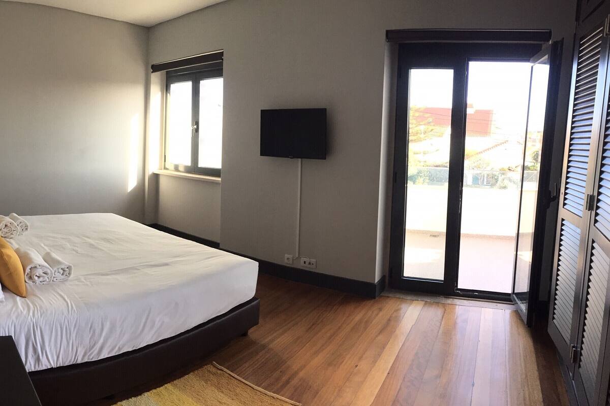A bedroom with a bed, a bedside table with a vase, a TV mounted on the wall, and a sliding glass door leading to an outdoor area.