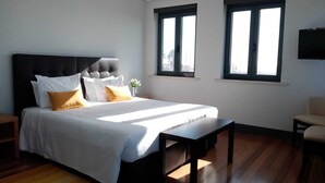 A bedroom with a large bed, two windows, a TV, and a wooden floor. - Villa Caparica Hostel (Almada)