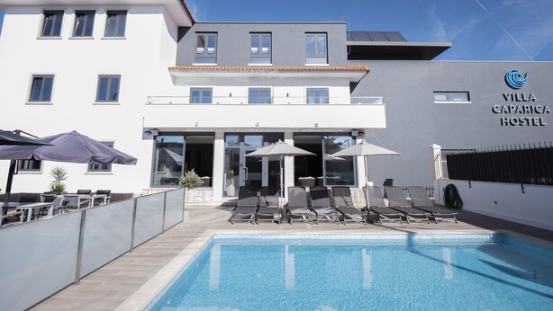 A modern hotel with a swimming pool, outdoor seating, and a clear sky. - Villa Caparica Hostel (Almada)