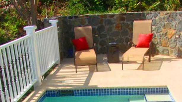 Piscina con escalones de acceso, rodeada por una valla blanca y dos sillas de descanso con cojines rojos.