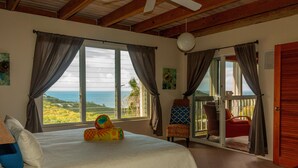 Un dormitorio con cama, vistas al océano y un balcón con sillas.