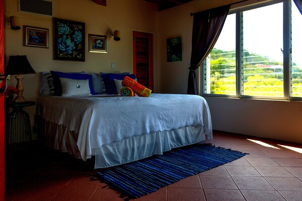 A bedroom with a bed, a window with curtains, and artwork on the walls. - Spacious, 3 Bed / 3 Bath, Pool, Screened Porch, Wi-Fi, A/C (Cruz Bay, St.John)