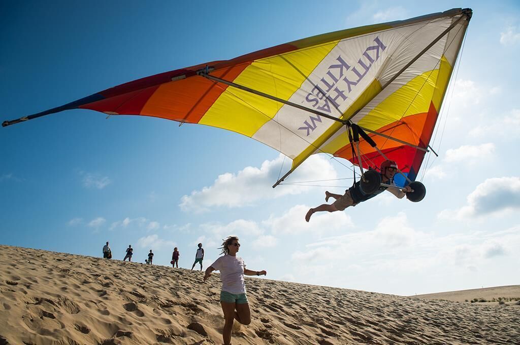 Eine Person in einem Harness wird von einem Kite einen sandigen Hügel hinaufgezogen.