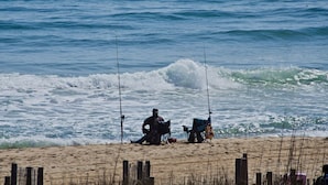 Ein Strand mit einer Person beim Angeln, einem Stuhl und einer Decke.