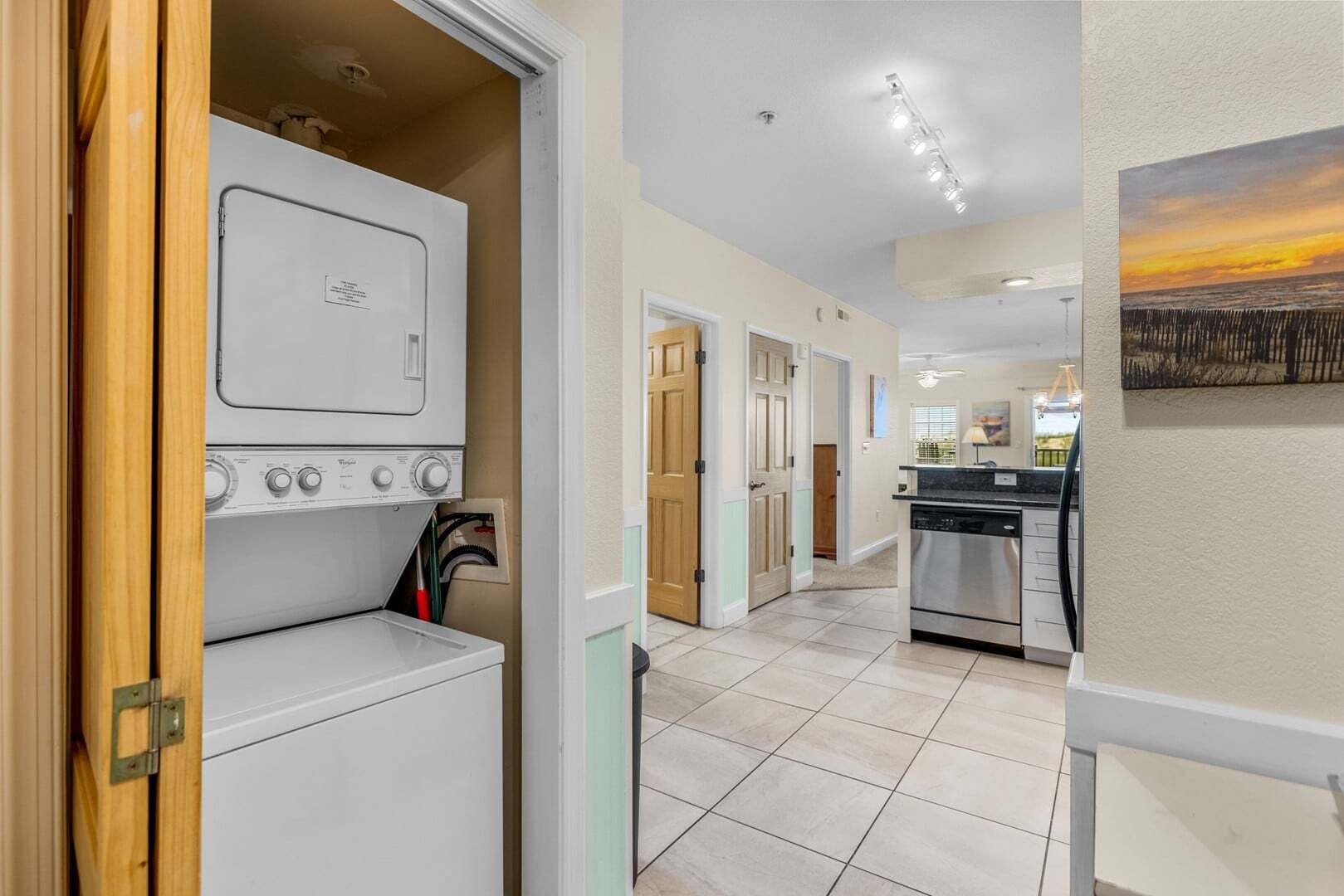 A laundry room with a washer and dryer, a hallway leading to a kitchen, and a painting on the wall.