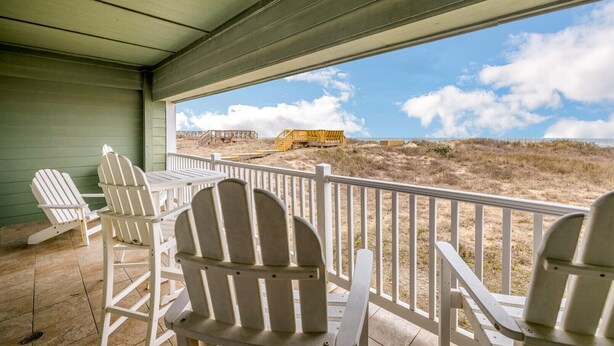 Eine überdachte Veranda mit weißen Adirondack-Stühlen und Blick auf den Strand.