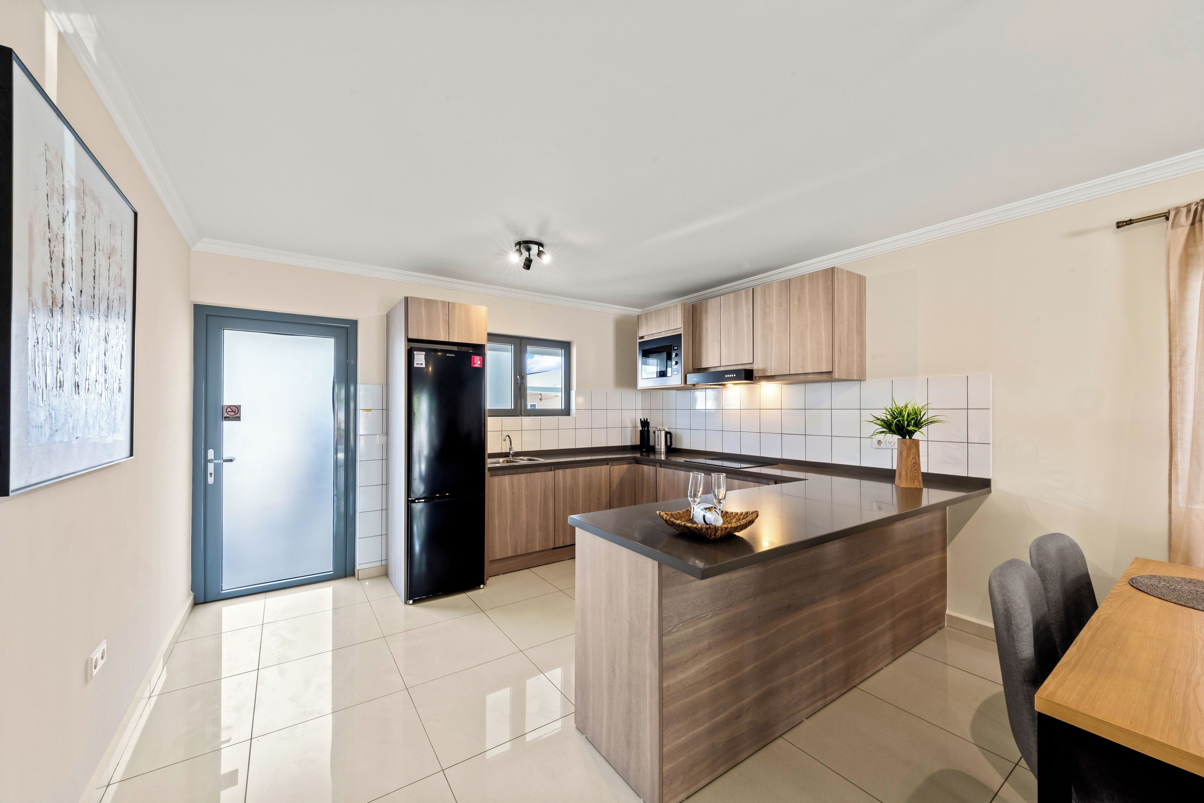 A modern kitchen with a central island, wooden cabinets, and a stainless steel refrigerator.