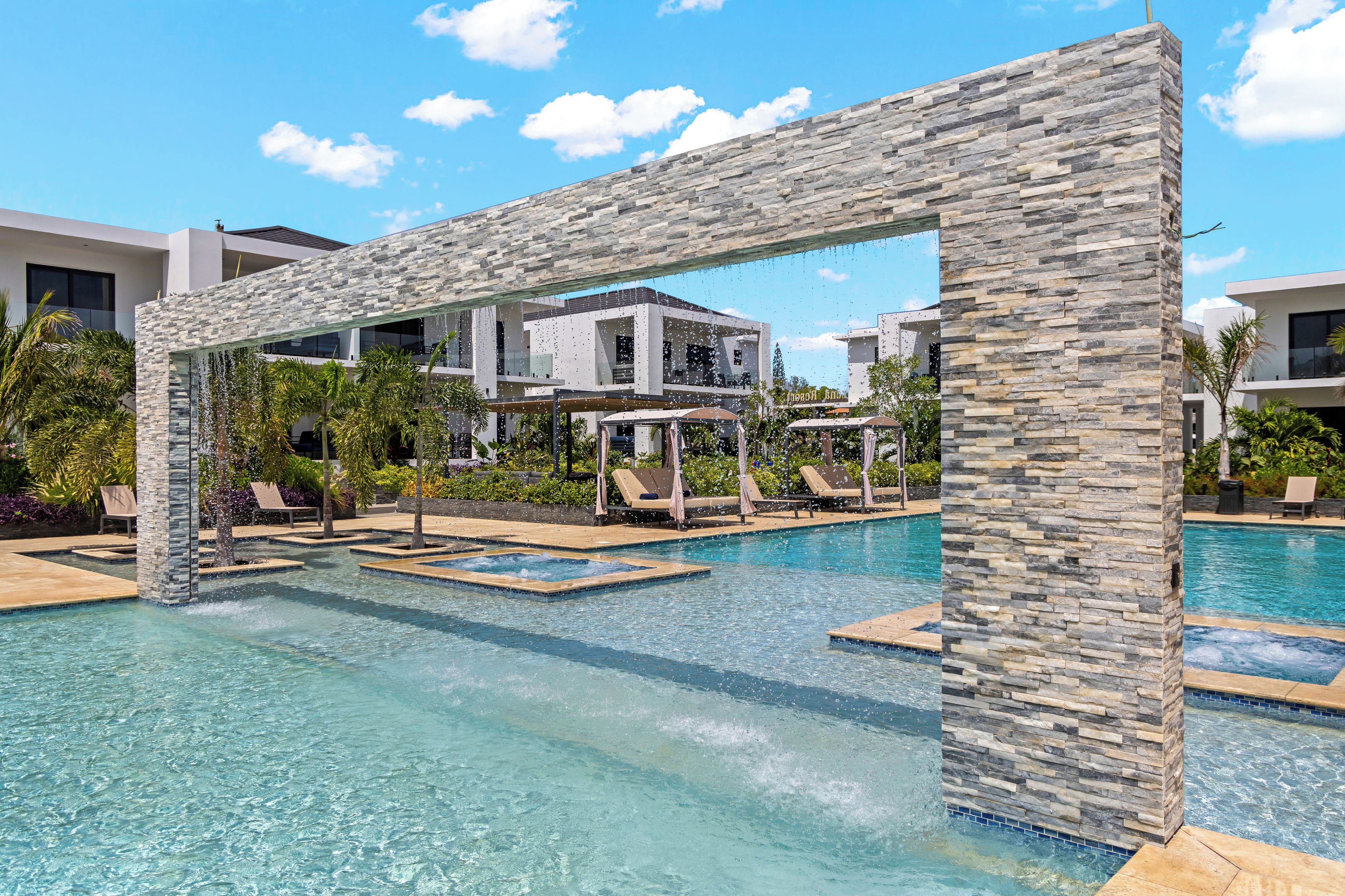 Una piscina con pilares de piedra, sillones de descanso y un edificio moderno al fondo.