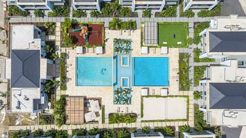 Vista aérea de un complejo turístico con dos piscinas, una zona de juegos para niños y una cancha de tenis.