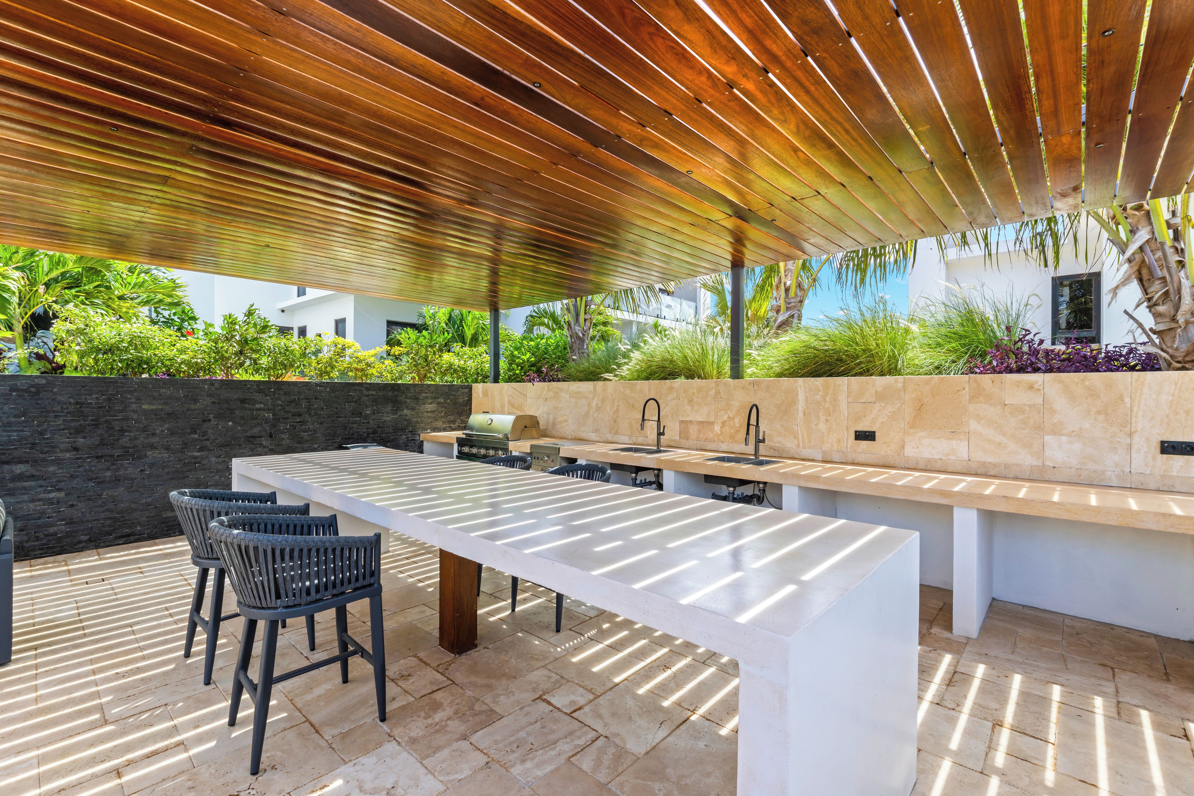 An outdoor kitchen area with a long countertop, bar stools, and a grill.