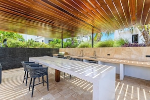 Un área de cocina al aire libre con una encimera larga, taburetes de bar y una parrilla.