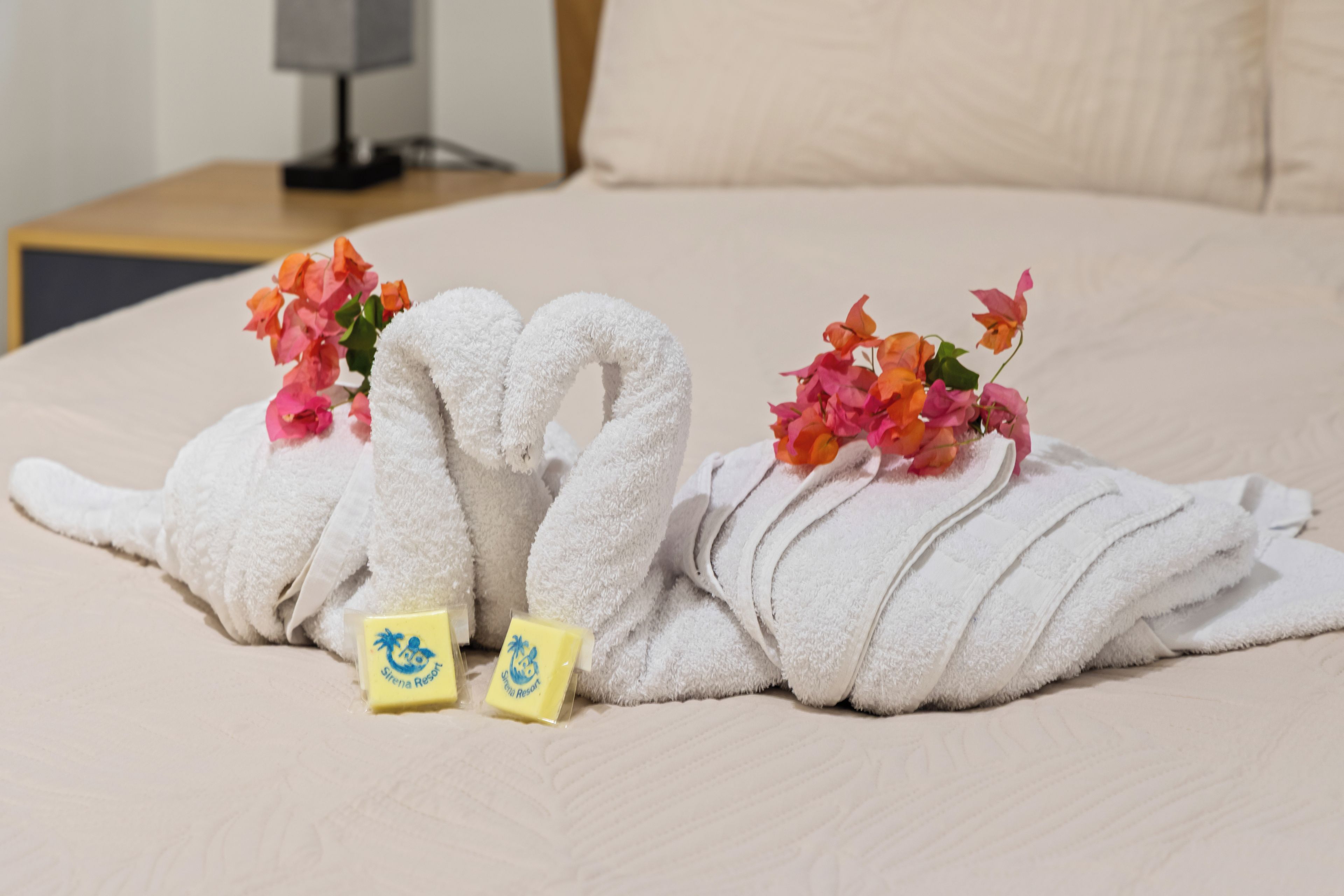 A neatly made bed with two towels shaped like swans, each adorned with flowers, and two small yellow soap bars.