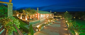 A well-lit, two-story building with a covered patio area, surrounded by landscaped gardens and a paved driveway.