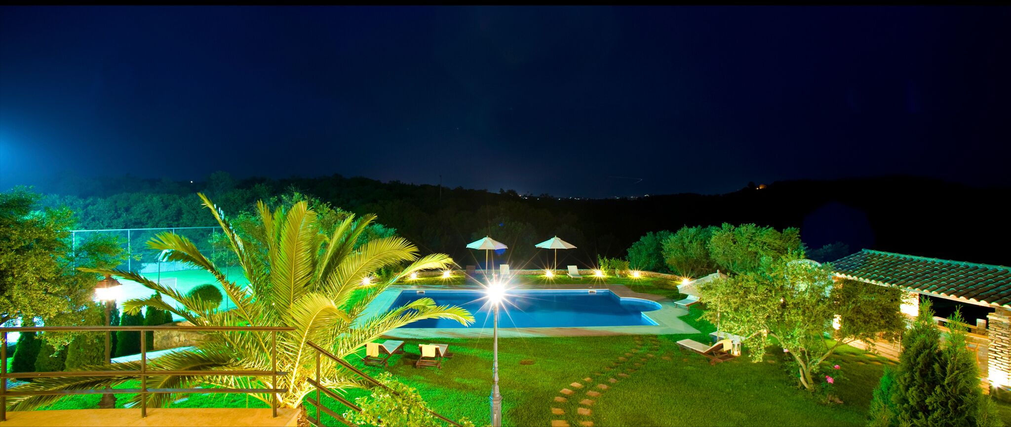 Une vue nocturne d’un complexe hôtelier avec une piscine, des chaises longues et des parasols.