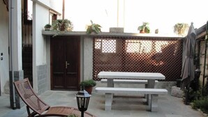 Un'area patio con una sedia di legno, una panchina e piante in vaso.