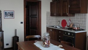 Una cucina con mobili in legno, zoccolo paraschizzi piastrellato, un fornello e un tavolo con un vasetto di frutta.