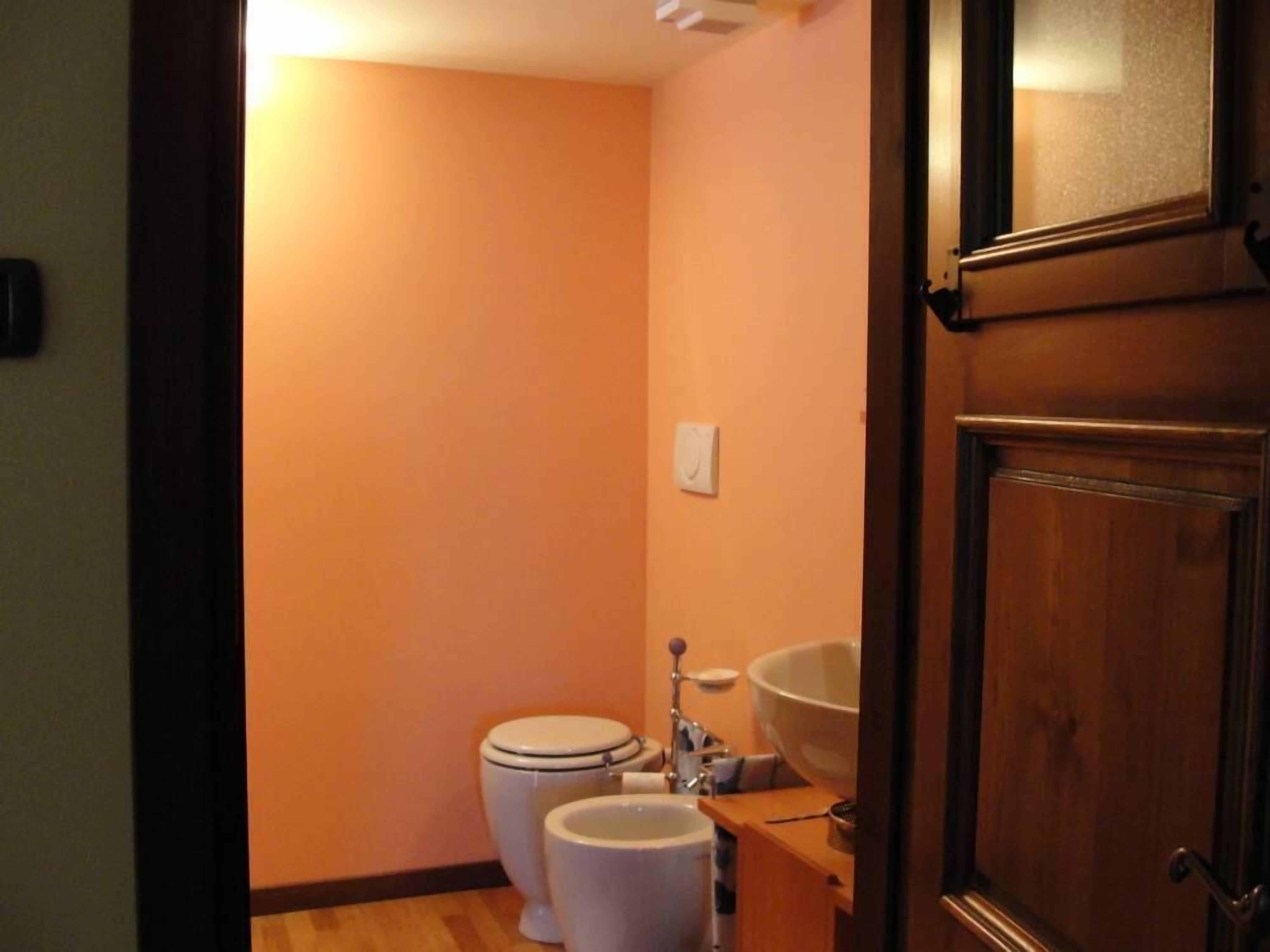 Une petite salle de bain avec un mur orange, des toilettes blanches et un lavabo blanc.