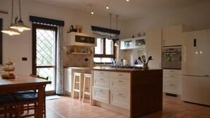 Une cuisine dotée d’un îlot central, de meubles blancs et d’un four encastré. On y trouve une fenêtre avec des rideaux et une porte qui donne sur une autre pièce.