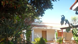 Una casa con porche cubierto, rodeada de plantas y árboles.