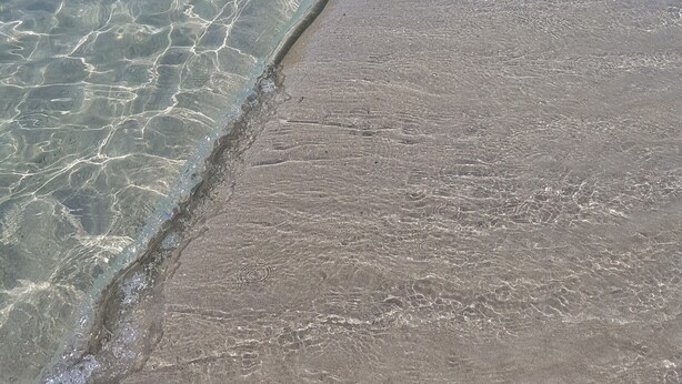 Una playa con aguas transparentes y poco profundas y una orilla arenosa.