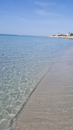 A beach with clear shallow waters and a sandy shore.