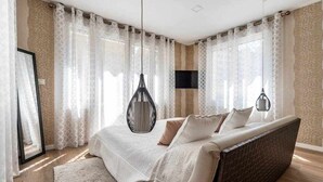 A bedroom with a bed, curtains, a hanging light fixture, and a mounted TV.