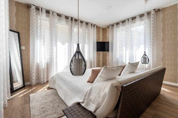 A bedroom with a bed, curtains, a hanging light fixture, and a mounted TV.