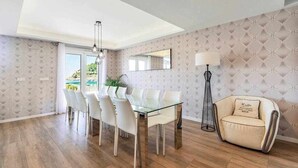 A modern dining area with a glass table and white chairs, a tufted wallpaper design, and a view through a glass door.