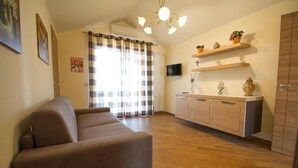 Een woonkamer met een bank, een keuken met houten kastjes, een televisie en een raam met gordijnen.
